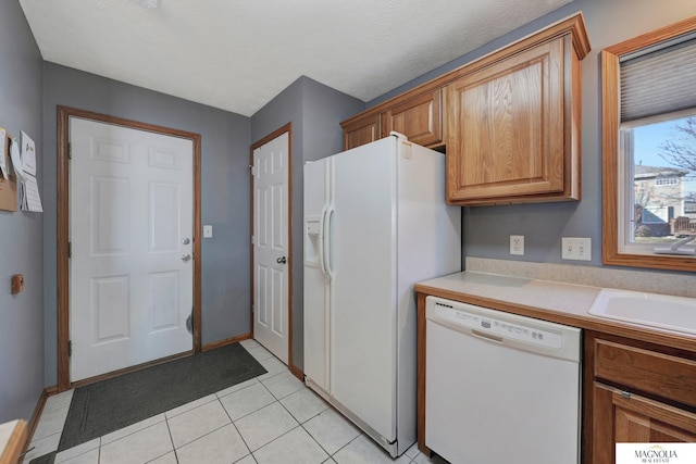 kitchen featuring light countertops, light tile patterned floors, brown cabinetry, white appliances, and a sink