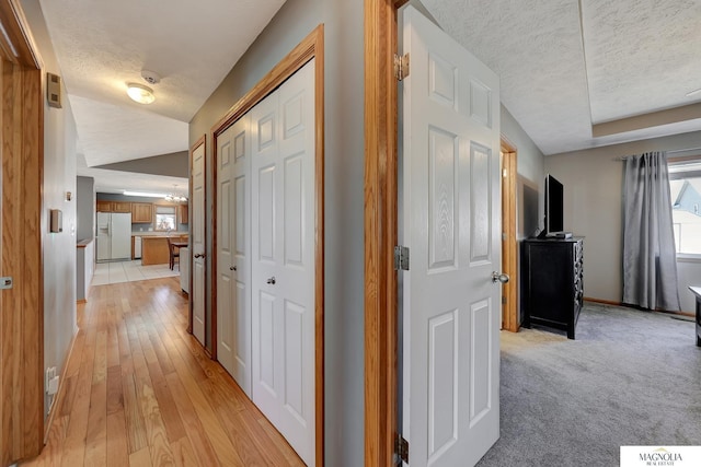 hall featuring light carpet, a textured ceiling, light wood finished floors, baseboards, and vaulted ceiling