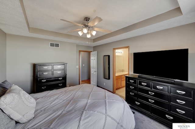 bedroom featuring ceiling fan, a tray ceiling, visible vents, and connected bathroom