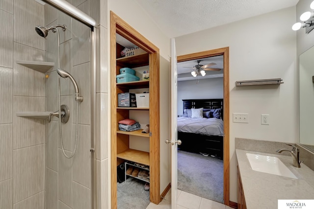 bathroom with a textured ceiling, connected bathroom, tile patterned flooring, tiled shower, and vanity