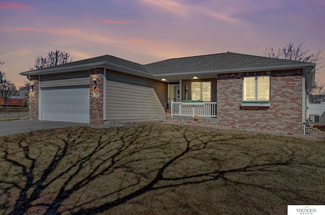 single story home with a lawn, a porch, concrete driveway, an attached garage, and brick siding