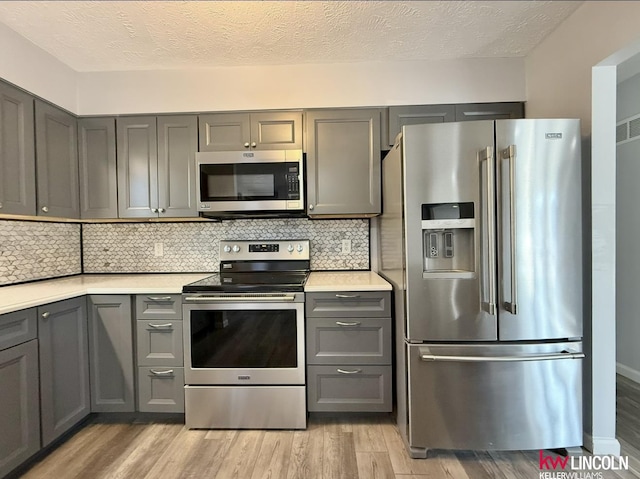 kitchen featuring stainless steel appliances, light countertops, decorative backsplash, gray cabinetry, and light wood-type flooring