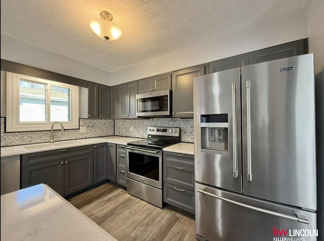 kitchen with stainless steel appliances, gray cabinets, light countertops, backsplash, and a sink