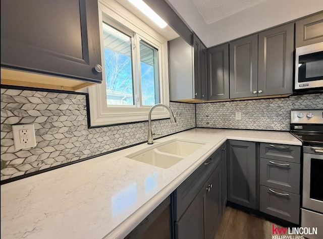 kitchen with appliances with stainless steel finishes, dark wood finished floors, a sink, and tasteful backsplash