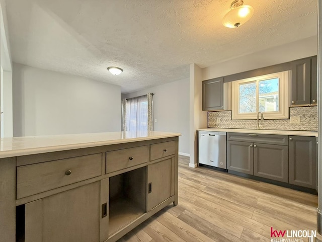 kitchen with light countertops, gray cabinetry, light wood-type flooring, stainless steel dishwasher, and a sink