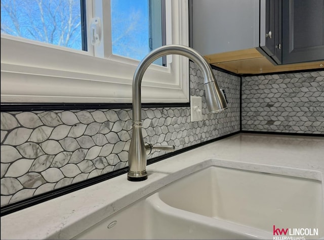 details featuring a sink, light stone counters, and backsplash