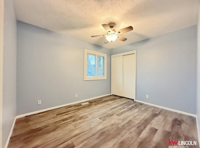 unfurnished bedroom featuring visible vents, baseboards, wood finished floors, a textured ceiling, and a closet