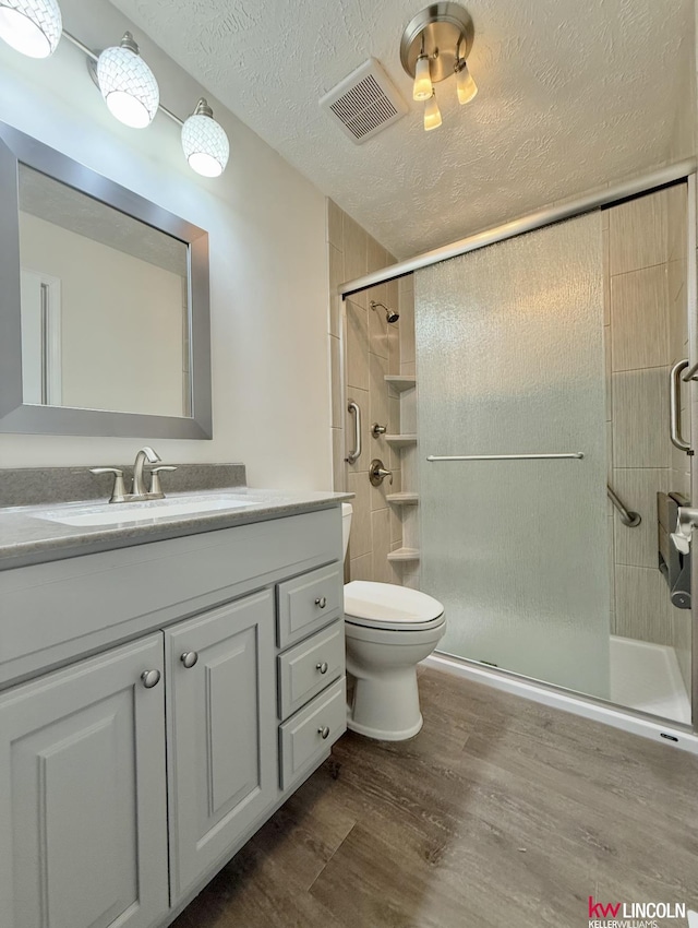 bathroom featuring a textured ceiling, wood finished floors, vanity, visible vents, and a shower stall