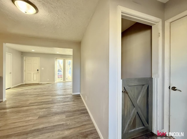 corridor with a textured ceiling, wood finished floors, and baseboards