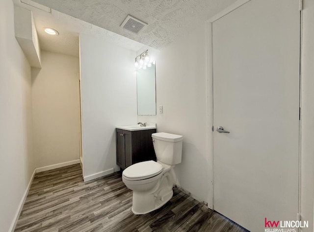 half bath with visible vents, toilet, vanity, a textured ceiling, and wood finished floors