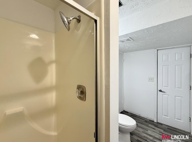 bathroom with a textured ceiling, toilet, wood finished floors, visible vents, and a shower stall