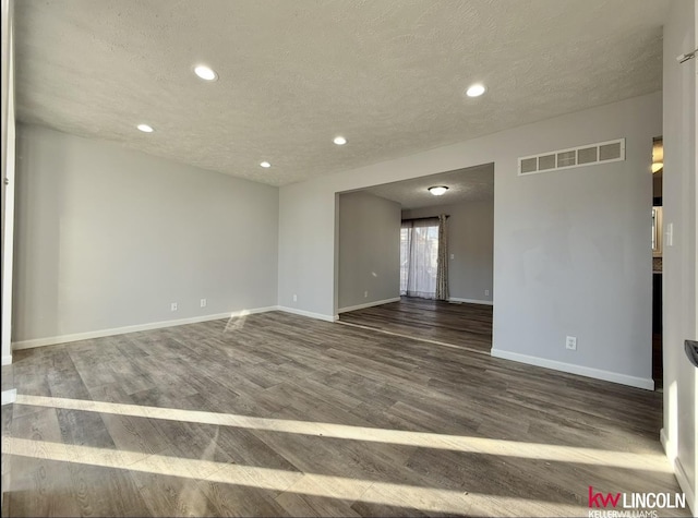 empty room with a textured ceiling, recessed lighting, dark wood-type flooring, visible vents, and baseboards