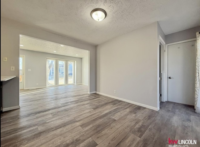 unfurnished living room with a textured ceiling, baseboards, and wood finished floors