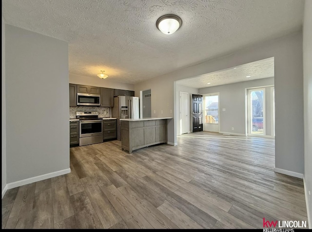 kitchen with open floor plan, stainless steel appliances, light countertops, light wood-type flooring, and backsplash