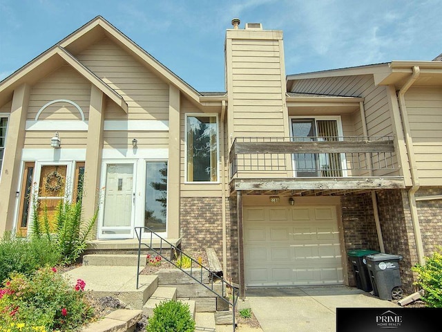 view of property featuring driveway, a balcony, a chimney, an attached garage, and brick siding