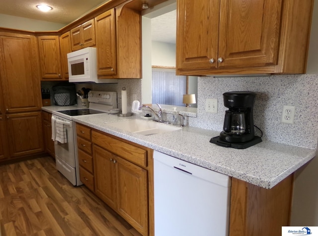 kitchen with backsplash, brown cabinets, wood finished floors, white appliances, and a sink