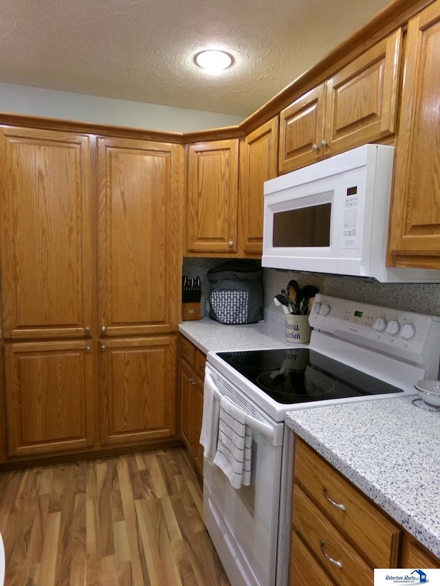 kitchen with light stone countertops, light wood-type flooring, brown cabinets, white appliances, and a textured ceiling