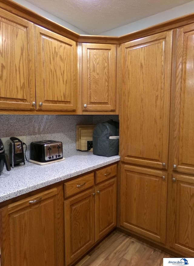 kitchen featuring light wood-type flooring, brown cabinets, and light stone countertops