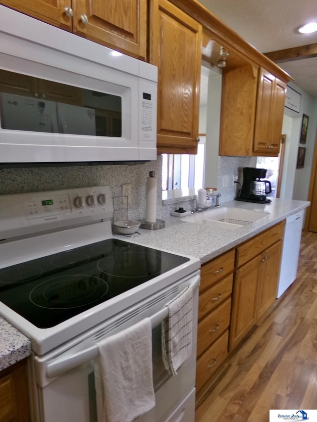 kitchen with white appliances, light wood-type flooring, a sink, tasteful backsplash, and brown cabinets