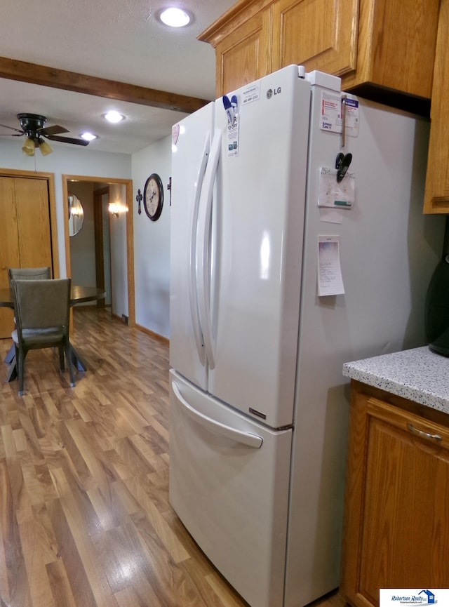 kitchen featuring light wood-type flooring, beamed ceiling, a ceiling fan, freestanding refrigerator, and light stone countertops