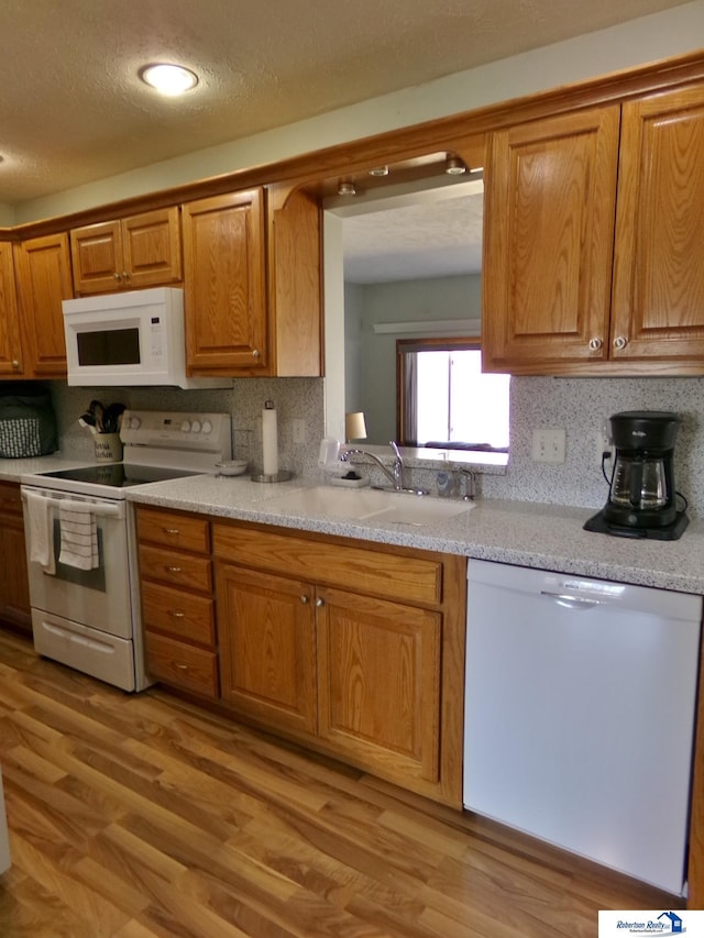 kitchen with white appliances, light wood finished floors, a sink, decorative backsplash, and light countertops