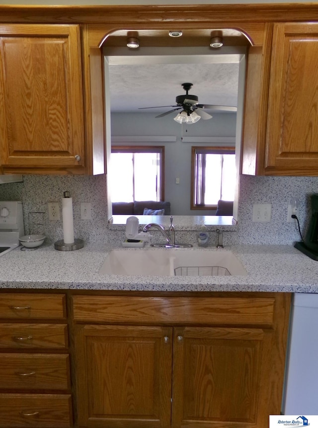 kitchen with a sink, light stone countertops, brown cabinets, and ceiling fan