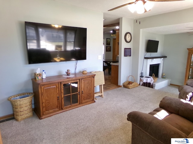 living room with visible vents, a fireplace with raised hearth, baseboards, ceiling fan, and carpet floors