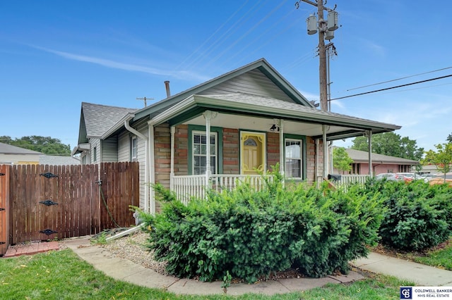 view of front facade featuring roof with shingles, a porch, and fence