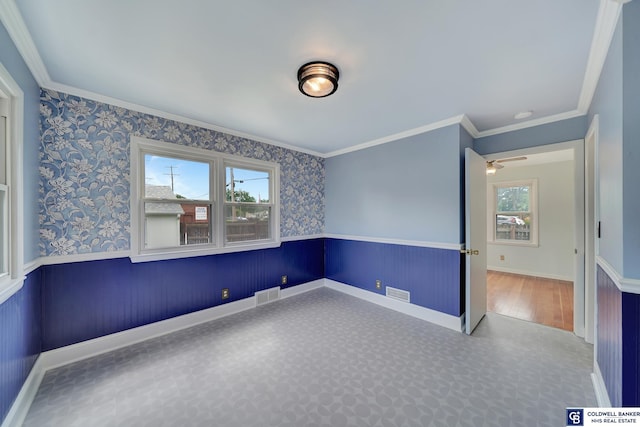 empty room featuring wallpapered walls, crown molding, visible vents, and wainscoting