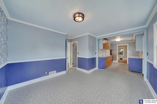 empty room with a wainscoted wall, light carpet, visible vents, and ornamental molding