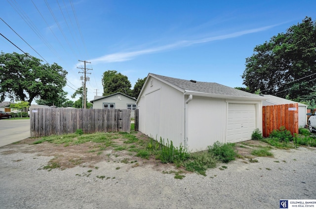 view of side of property with a shingled roof, a detached garage, an outdoor structure, and fence