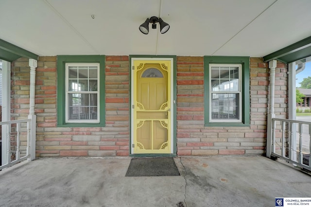 doorway to property with brick siding, stone siding, and covered porch