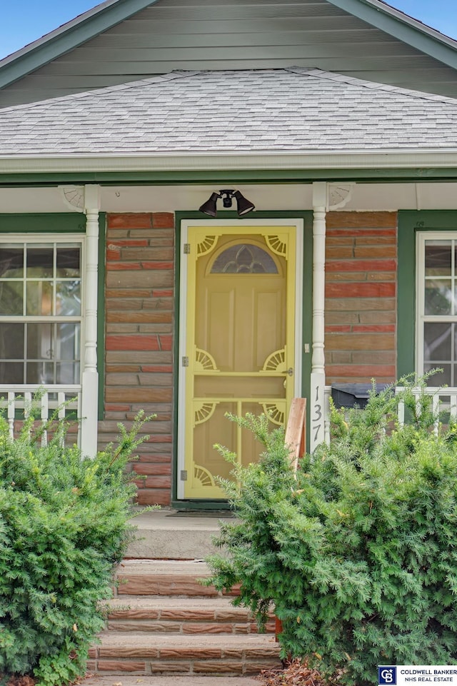 view of exterior entry featuring covered porch and roof with shingles