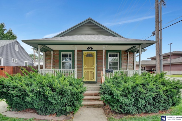 view of front of home featuring fence, covered porch, and a shingled roof