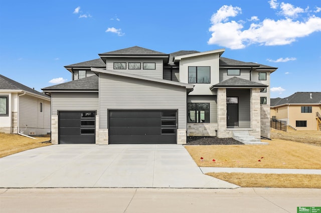 prairie-style house with stone siding, concrete driveway, a shingled roof, and an attached garage