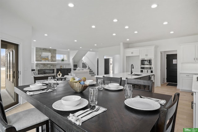 dining space featuring light wood-type flooring, recessed lighting, stairway, and a tile fireplace