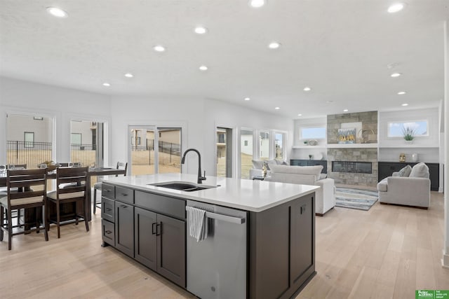 kitchen with a sink, light wood-type flooring, a fireplace, and stainless steel dishwasher