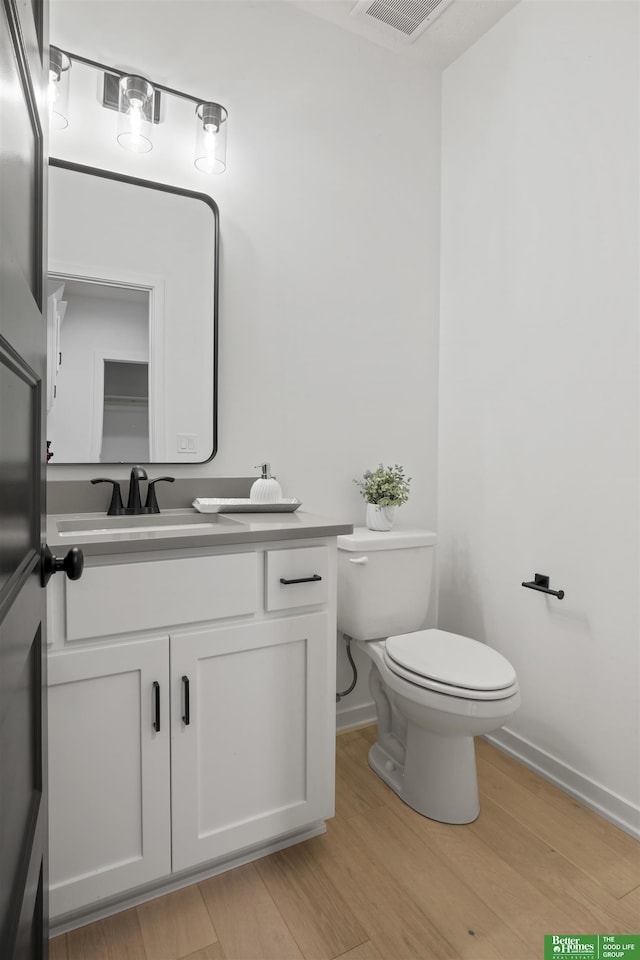 half bath featuring visible vents, vanity, wood finished floors, and toilet