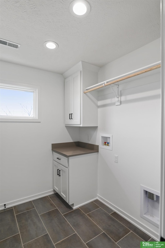 laundry area with a textured ceiling, hookup for a washing machine, visible vents, baseboards, and cabinet space