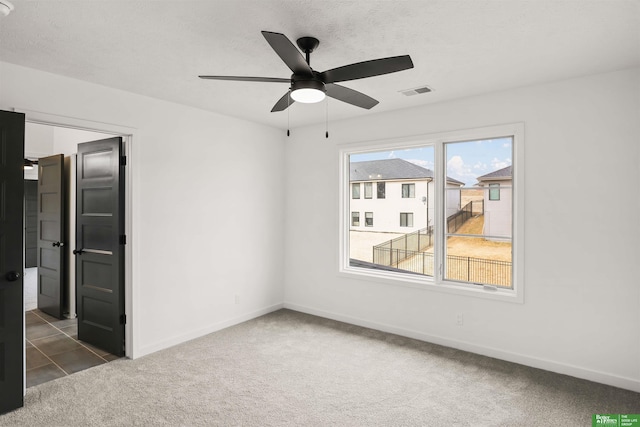 carpeted empty room featuring a textured ceiling, ceiling fan, visible vents, and baseboards