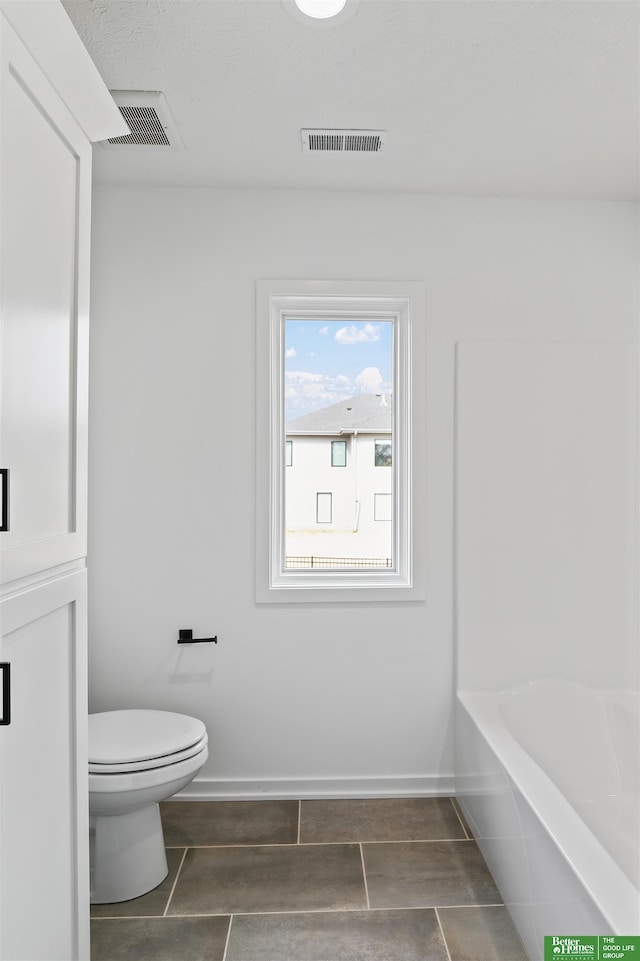 bathroom with toilet, baseboards, a tub to relax in, and visible vents