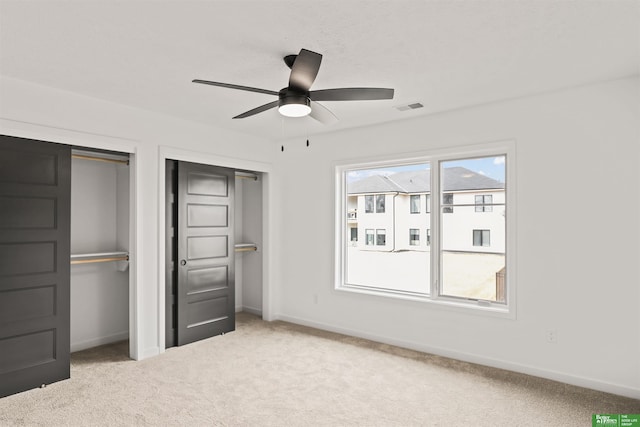 unfurnished bedroom with baseboards, carpet, visible vents, and two closets