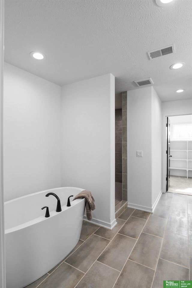 full bathroom with visible vents, a freestanding bath, a textured ceiling, tiled shower, and baseboards