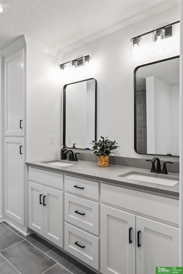 bathroom with a textured ceiling, double vanity, a sink, and tile patterned floors