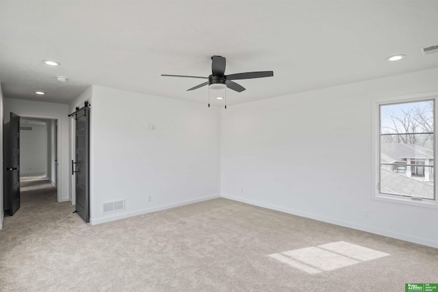 unfurnished room featuring a barn door, visible vents, baseboards, and light colored carpet