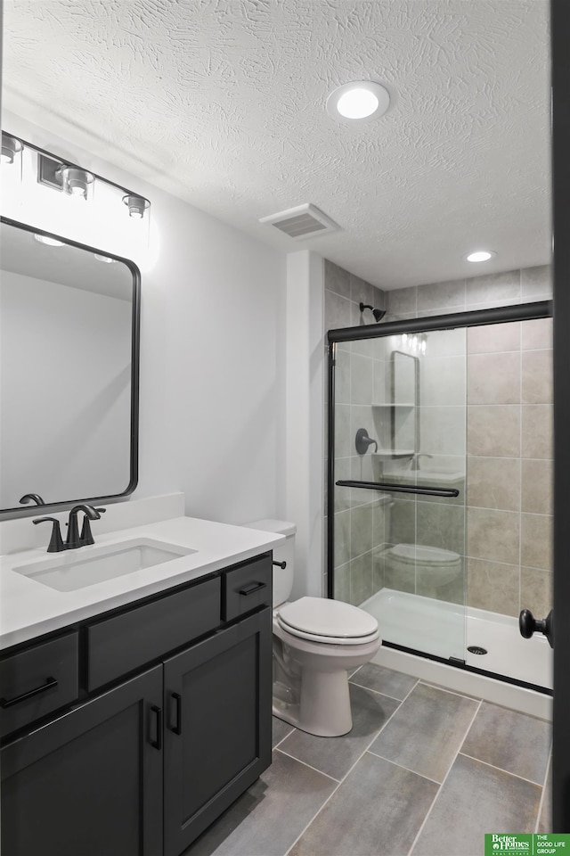 bathroom featuring a textured ceiling, toilet, visible vents, vanity, and a stall shower