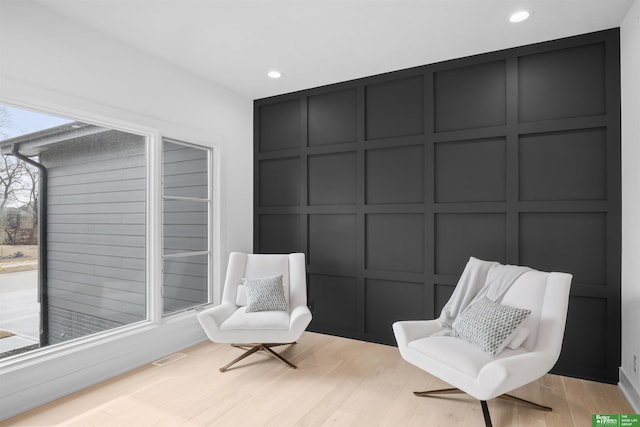 sitting room featuring light wood-style floors, recessed lighting, visible vents, and a decorative wall