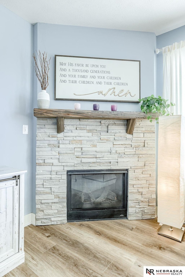 room details with a stone fireplace, a textured ceiling, and wood finished floors