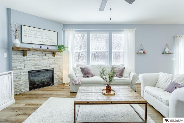 living room with light wood-type flooring, ceiling fan, and a stone fireplace