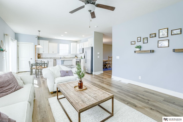 living room featuring light wood-style floors, ceiling fan, baseboards, and recessed lighting